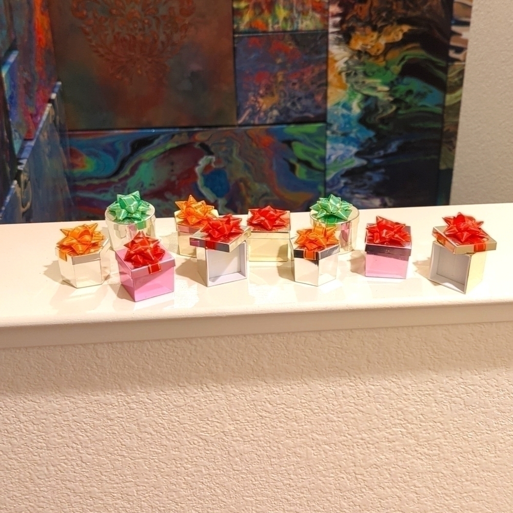 10 adorable tiny ring boxes in gold, pink, and silver with colored bows on top.